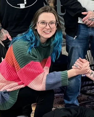Katie Connor, smiling, with blue hair and a striped sweater